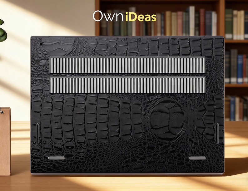 May include: Black laptop skin with a crocodile texture. The skin has two silver-colored vent strips and the text "OwniIdeas" in the upper left corner. The laptop skin is on a wooden surface.