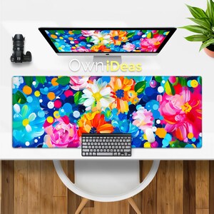 May include: A colorful floral design desk mat with a blue background and a keyboard on top of it. The design features bright pink, yellow, orange, and white flowers with blue and white circles.