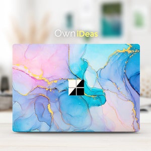 Puede incluir: Una piel para portátil con un diseño abstracto de mármol en tonos azules, rosas y dorados. La piel tiene un recorte para la cámara del portátil y un acento dorado alrededor de los bordes.