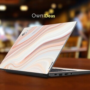 May include: A closed laptop computer with a white, orange, and brown marble pattern on the lid. The laptop has the word "Lenovo" on the bottom right corner of the lid. The laptop is sitting on a wooden surface.