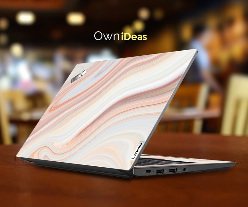 May include: A closed laptop computer with a white, orange, and brown marble pattern on the lid. The laptop has the word "Lenovo" on the bottom right corner of the lid. The laptop is sitting on a wooden surface.