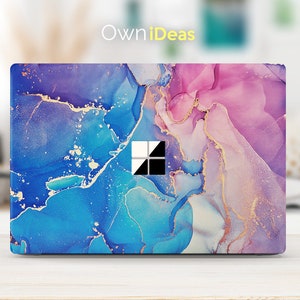 Puede incluir: Piel para portátil con un diseño abstracto de mármol en tonos azules, morados y rosas con detalles dorados. La piel tiene el logotipo de Windows en el centro.