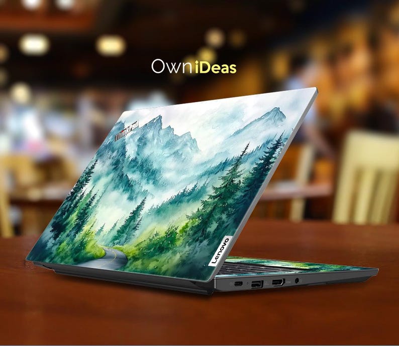 May include: A laptop computer with a watercolor design of a mountain range with a road winding through it. The design is in shades of blue, green, and white. The laptop is closed and the design is on the top of the lid. The laptop brand is Lenovo.