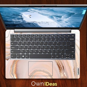 Op de afbeelding: Een laptop met een wit en gouden marmerontwerp op de deksel en het toetsenbord. De laptop is gesloten en het scherm toont een besneeuwde berg sc&egrave;ne. De tekst "Own iDeas" is onderaan de afbeelding gedrukt.