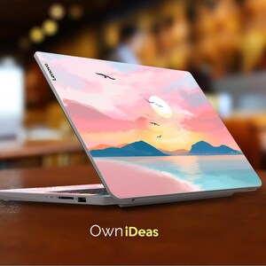 Op de afbeelding: Een Lenovo laptop met een aangepaste skin met een zonsondergang boven de oceaan. Het ontwerp toont een roze en oranje lucht, blauwe bergen en vliegende vogels. De tekst "OwniDeas" staat onderaan.