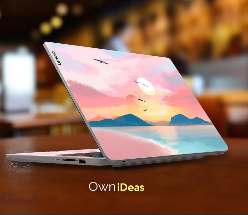 Op de afbeelding: Een Lenovo laptop met een aangepaste skin met een zonsondergang boven de oceaan. Het ontwerp toont een roze en oranje lucht, blauwe bergen en vliegende vogels. De tekst "OwniDeas" staat onderaan.