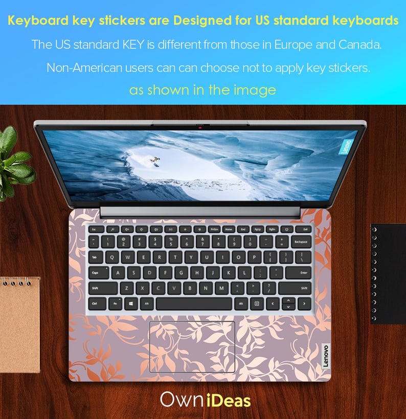 Op de afbeelding: Een Lenovo-laptop met een bloemen toetsenbord skin. De skin heeft een lavendel achtergrond met oranje en witte bladmotieven. Het scherm toont een landschapsafbeelding. Bovenin staat: "Keyboard key stickers are Designed for US standard keyboards."