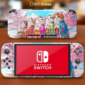 May include: A pink and white Nintendo Switch console skin featuring a design of four cats wearing traditional Japanese clothing in front of a cherry blossom tree. The text "OwnIdeas" is printed at the top of the skin.