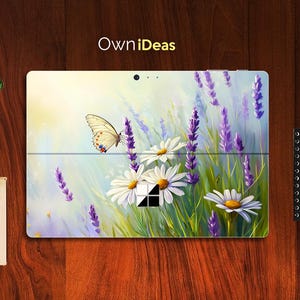 Puede incluir: Una piel para portátil con un diseño floral que presenta una mariposa, margaritas y lavanda. El diseño está sobre un fondo blanco con un degradado azul claro.