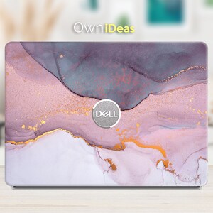 Puede incluir: Una funda para portátil con un diseño abstracto en tonos morado, rosa y dorado. El diseño tiene un efecto marmolado con líneas fluidas y un acento dorado metálico. El logotipo de Dell es visible.