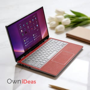 K&ouml;nnte beinhalten: Ein silberner Laptop mit einer roten strukturierten Oberfl&auml;che auf Tastatur und Touchpad. Der Bildschirm zeigt eine violett-orangefarbene Oberfl&auml;che. Der Laptop ist auf einer wei&szlig;en Oberfl&auml;che ge&ouml;ffnet, mit dem Text "OwniDeas".