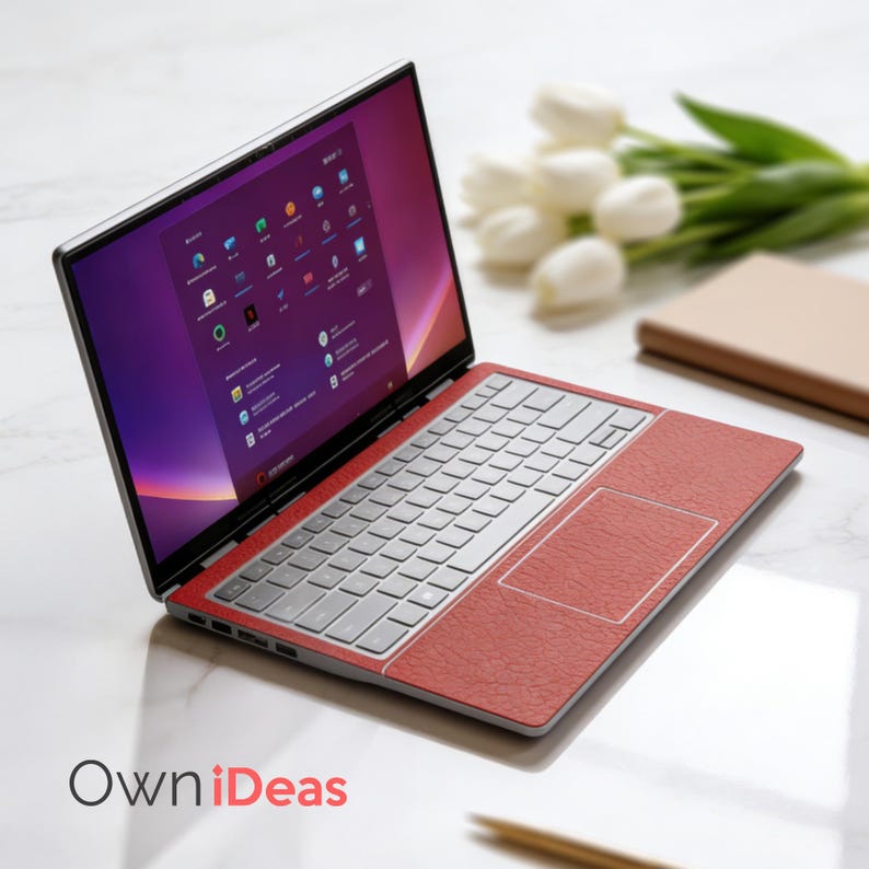 K&ouml;nnte beinhalten: Ein silberner Laptop mit einer roten strukturierten Oberfl&auml;che auf Tastatur und Touchpad. Der Bildschirm zeigt eine violett-orangefarbene Oberfl&auml;che. Der Laptop ist auf einer wei&szlig;en Oberfl&auml;che ge&ouml;ffnet, mit dem Text "OwniDeas".