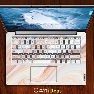 May include: A laptop computer with a white marble design on the lid and keyboard. The laptop is open and the screen is showing a snowy mountain scene. The keyboard has a white background with black keys and the text "Lenovo" is visible on the bottom right corner of the laptop.