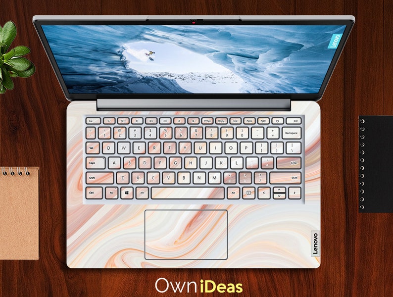 May include: A laptop computer with a white marble design on the lid and keyboard. The laptop is open and the screen is showing a snowy mountain scene. The keyboard has a white background with black keys and the text "Lenovo" is visible on the bottom right corner of the laptop.