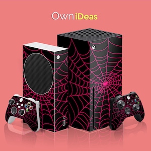 Puede incluir: Dos consolas Xbox Series X negras con diseños de telaraña rosa y mandos a juego. Las consolas están una al lado de la otra y los mandos están a cada lado de las consolas.