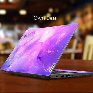 May include: A purple and gold laptop skin with a galaxy-like design. The skin features swirling clouds of purple and pink with gold accents. The laptop skin is designed to fit a Lenovo laptop.