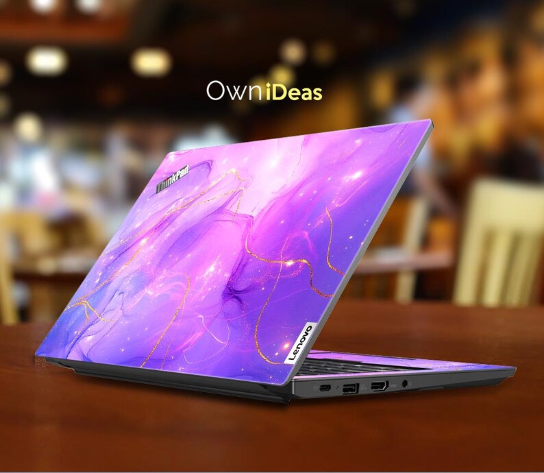 May include: A purple and gold laptop skin with a galaxy-like design. The skin features swirling clouds of purple and pink with gold accents. The laptop skin is designed to fit a Lenovo laptop.