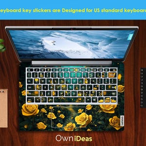 Puede incluir: Un ordenador port&aacute;til con una pegatina de teclado que presenta una escena de bosque oscuro verde y negro con rosas amarillas y luces brillantes. El texto "OwnIdeas" est&aacute; impreso debajo del teclado.