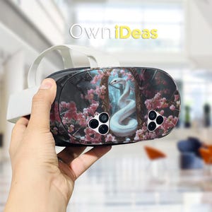 以下が含まれることがあります： ピンクの桜の花の中で白いヘビを描いたカスタムスキンを備えたVRヘッドセット。ヘッドセットは、複数のカメラレンズを備えた白黒のデザインです。「OwniDeas」というテキストが表示されます。