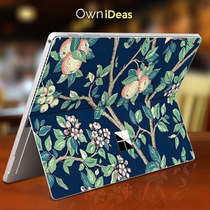 Puede incluir: Una piel para portátil azul con un patrón floral que presenta flores blancas, hojas verdes y fruta rosa y amarilla. La piel está diseñada para un portátil Microsoft Surface.
