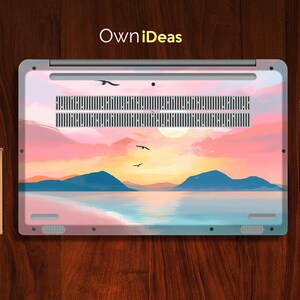 Op de afbeelding: Laptop skin met een zonsondergang, met een levendige lucht in roze, oranje en geel. Het ontwerp toont silhouetten van bergen, water en vogels in vlucht. De tekst "OwniDeas" is rechtsboven zichtbaar.