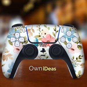 May include: A white PlayStation 5 controller with a floral design featuring pink, blue, and green flowers. The controller has a black rubber grip and buttons. The text "OwnIdeas" is printed on the bottom of the controller.