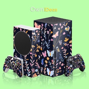 以下が含まれることがあります： 花柄と蝶の模様が施されたXbox Series Xが2台。左側のコンソールはディスク版、右側のコンソールはデジタル版です。両方のコンソールは、ピンク、ブルー、イエローの花と蝶が描かれた黒い背景になっています。