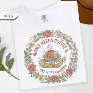May include: White t-shirt with a floral wreath design. The design includes the text "MAMA NEEDS COFFEE & ONE MORE CHAPTER" around a coffee cup and books. The shirt is labeled "COMFORT COLORS" and size L-G-G.