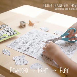 Child cutting out black-and-white animal shapes with scissors from a printable activity page, with the “Animals of Australia” book visible on a wooden desk, labeled as a digital download printable.