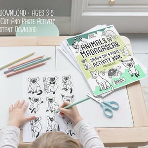 May include: A child coloring a printable cut and paste activity sheet featuring lemurs and other animals. The activity book, titled "Animals of Madagascar," is open on a white table with colored pencils and scissors. Text on the image reads "Digital Download, Ages 3-5."