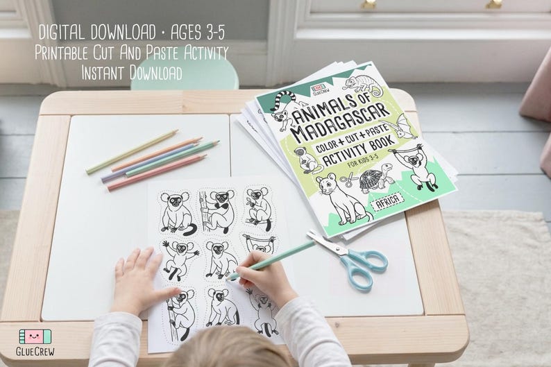 May include: A child coloring a printable cut and paste activity sheet featuring lemurs and other animals. The activity book, titled "Animals of Madagascar," is open on a white table with colored pencils and scissors. Text on the image reads "Digital Download, Ages 3-5."