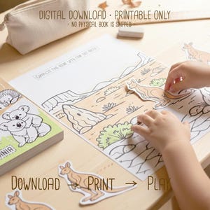Child placing cut-out kangaroo pieces onto a printed Australia desert scene page, with the “Animals of Australia” activity book visible on a wooden desk, labeled as a digital download printable.