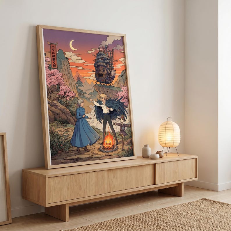 May include: Framed art print featuring a scene from a Japanese animated film. The artwork depicts characters in a mountain landscape with a castle, a bonfire, and cherry blossoms. The color palette includes shades of orange, blue, and pink.