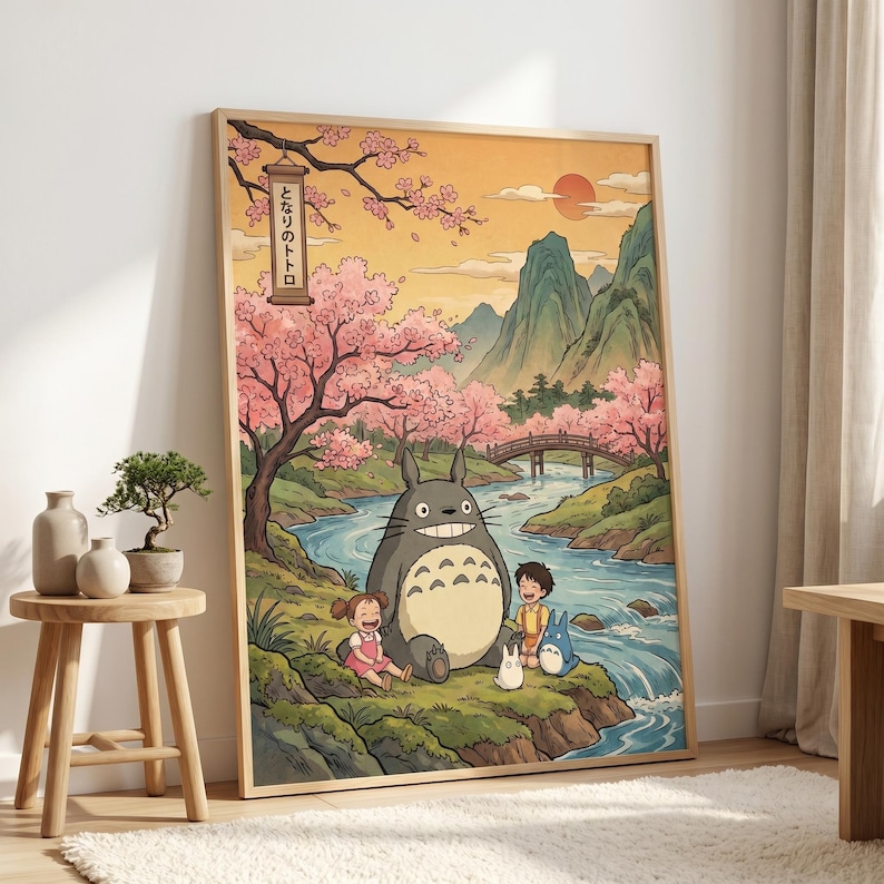 May include: A framed art print featuring a scene from the animated film, My Neighbor Totoro. The artwork depicts Totoro with two children near a river, under cherry blossom trees. The background includes mountains, a bridge, and a setting sun. The Japanese text is visible.