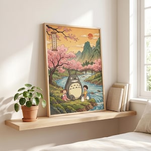 May include: Framed art print featuring a scene from the animated film "My Neighbor Totoro." The artwork depicts Totoro with two children near a river, under cherry blossom trees. The background includes mountains, a bridge, and a setting sun.