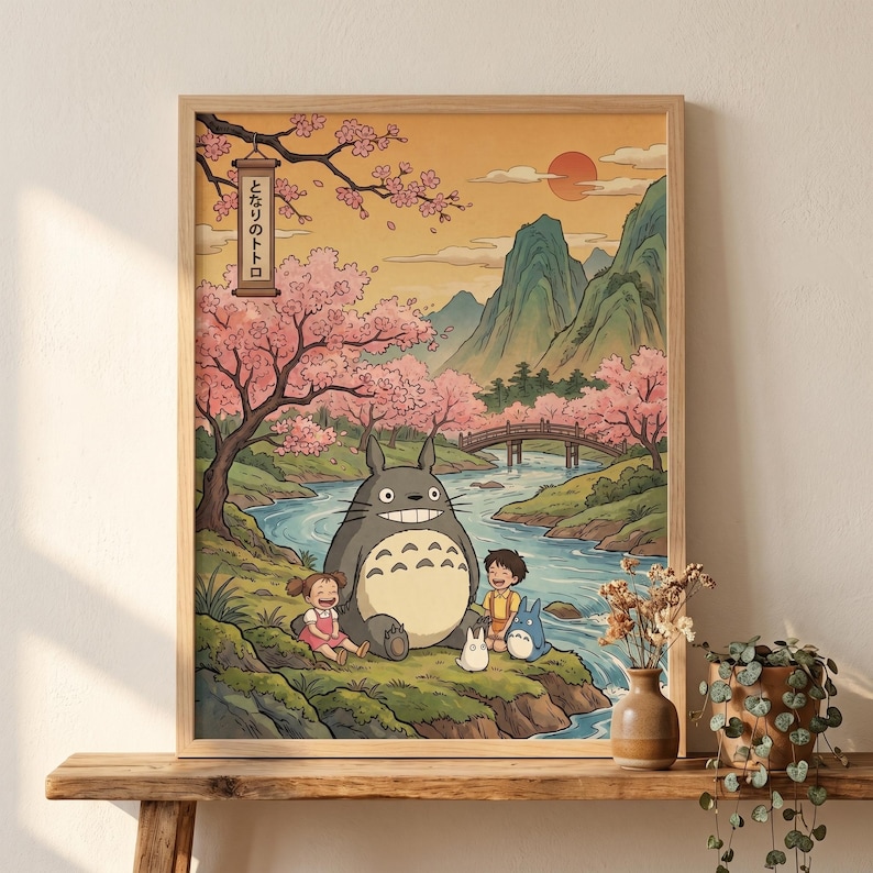 May include: A framed print featuring a scene from the animated film, My Neighbor Totoro. The artwork depicts Totoro, two children, and two smaller Totoros near a river, with a bridge, mountains, and cherry blossom trees in the background. The text "となりのトトロ" is visible.