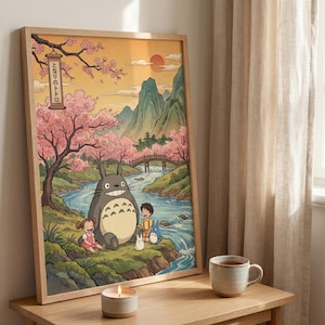 May include: A framed print featuring a scene with a large gray Totoro character, two children, and smaller Totoros near a river. The background includes a bridge, mountains, cherry blossom trees, and a setting sun. The frame is light wood.