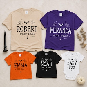 May include: A collection of five short-sleeved shirts and one bodysuit in beige, purple, orange, black, and white. Each garment features Halloween-themed graphics including bats, spiderwebs, and spiders, with personalized names and text like Spooky Squad.