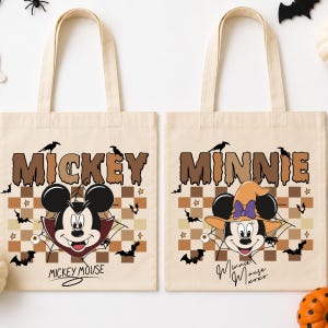 May include: Two beige canvas tote bags featuring Halloween-themed graphics. The left bag shows Mickey Mouse as a vampire with the text MICKEY and MICKEY MOUSE. The right bag shows Minnie Mouse in a witch hat with the text MINNIE and Minnie Mouse xoxo.