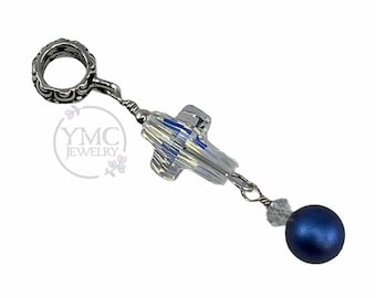 May include: A silver-toned charm with a decorative ring, a clear crystal cross, and a dark blue bead. The charm is designed for jewelry making and features a unique, eye-catching design.