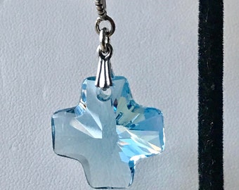 May include: A silver charm with a light blue crystal cross pendant. The charm is attached to a white ribbon.