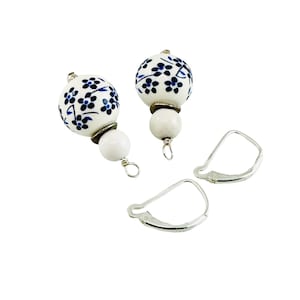 May include: A pair of white ceramic earrings with blue floral designs. The earrings have silver leverback closures.