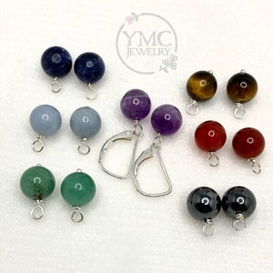 May include: A set of 10 gemstone earrings with silver ear wires. The gemstones are in various colors, including blue, green, purple, red, and brown. The earrings are arranged in pairs on a white surface.