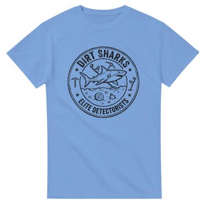 May include: A light blue short-sleeve t-shirt featuring a black circular graphic on the chest. The design includes a shark, metal detectors, a pickaxe, a coin, and a ring, with the text DIRT SHARKS ELITE DETECTORISTS printed in a circular border.
