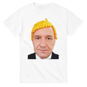 May include: A white short-sleeve t-shirt featuring a centered graphic print of a person with a neutral expression wearing a wig made of bright yellow cheese puffs. The person is dressed in a black suit jacket and a white collared shirt underneath.