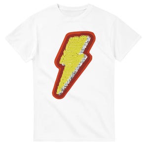 May include: White t-shirt with a yellow sequined lightning bolt design, outlined in red. The lightning bolt has a silver border. This casual t-shirt is suitable for everyday wear.