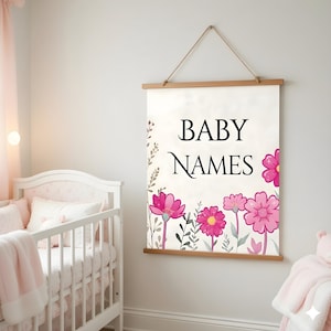May include: A rectangular wall hanging with the words "BABY NAMES" in black script. The bottom of the sign features pink flowers and green leaves. The sign is suspended by a wooden rod and a natural rope.
