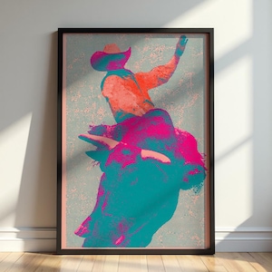 May include: A framed wall art print featuring a stylized graphic illustration of a cowboy riding a bucking bull. The artwork uses a vibrant color palette of teal, magenta, and orange with a distinct halftone dot pattern throughout the design.