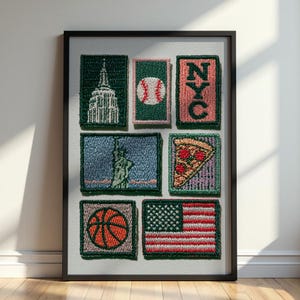 May include: A framed collection of seven rectangular embroidered patches featuring New York City themes, including the Empire State Building, a baseball, the letters NYC, the Statue of Liberty, a slice of pizza, a basketball, and the American flag.