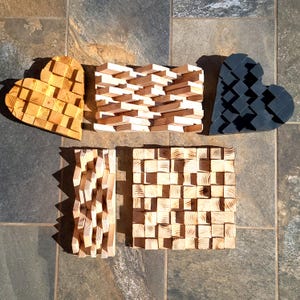 Peut inclure: Plusieurs œuvres d'art en bois, dont deux sculptures en forme de cœur et deux panneaux rectangulaires. Les cœurs sont faits de blocs imbriqués, l'un en bois naturel et l'autre en gris foncé. Les pièces rectangulaires présentent des motifs géométriques texturés.